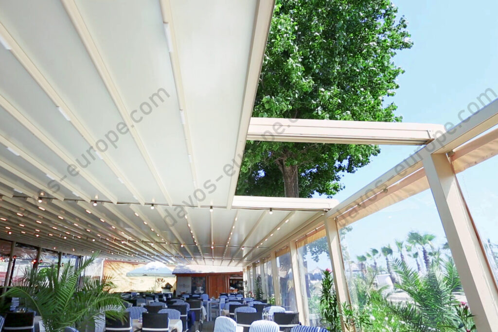 Pergola textila Davos de culoare crem montata pe terasa unui restaurant. Partial deschisa, vedere din interior.