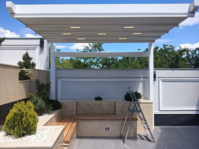 Pergola textila Davos de culoare alba montata in curtea unei case, deasupra unei canepele.